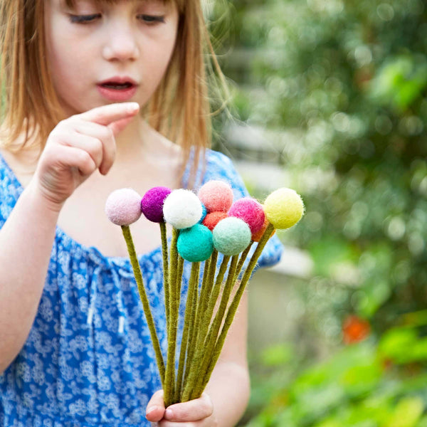 Child holding a bouquet of colourful felt pom pom flowers outdoors