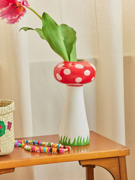 Red and white polka dot vase with a green base on a wooden table, featuring a pink tulip.
