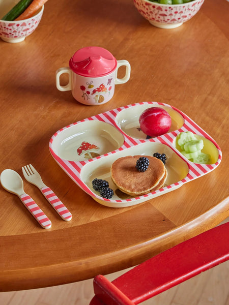 Children's meal set with pancakes, fruit, and cutlery on a wooden table