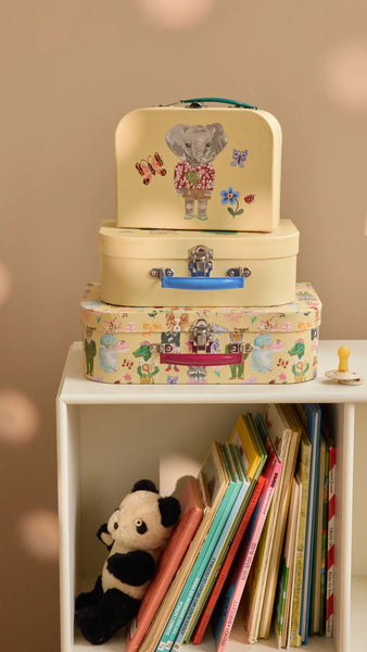 Stack of children's suitcases with animal designs on a shelf with books and a plush toy.