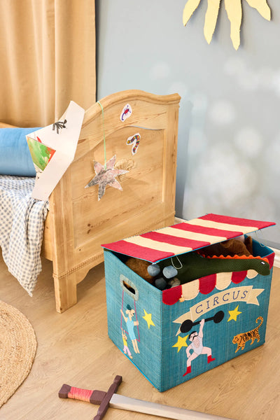 Toy storage box with circus design next to a wooden bed in a child's room.