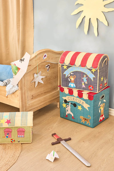 Children's toy storage boxes with circus design on a wooden floor next to a bed.