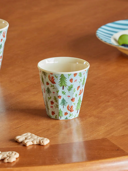 Patterned cup on a wooden table with cookies and a plate in the background