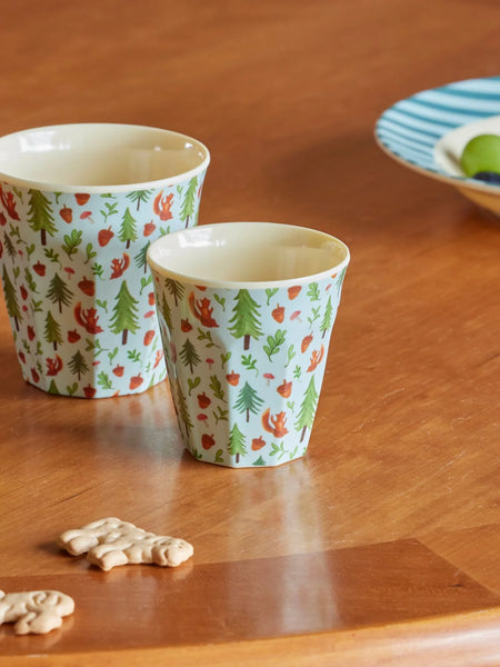 Two patterned cups on a wooden table with cookies.