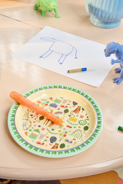 Children's plate with animal illustrations, carrot and colouring book on a table