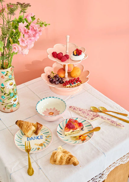 Table setting with pastries, fruit, and a two-tiered stand against a pink background
