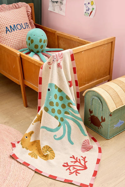 Green octopus soft toy in a child's bed with matching blanket