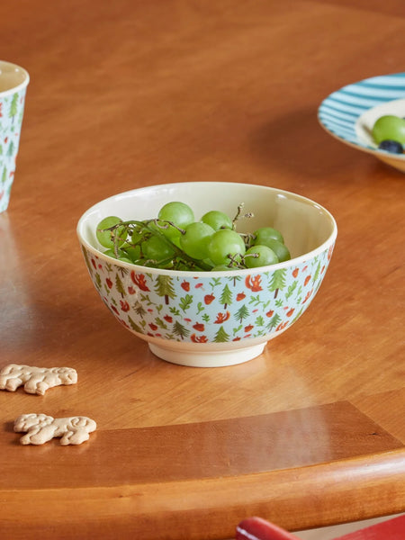 Decorative bowl with a forest pattern containing green grapes on a wooden table.