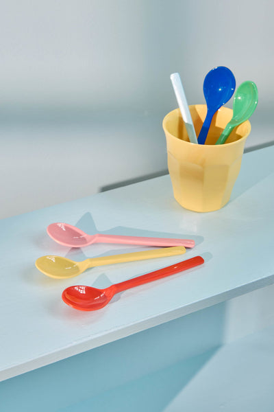 Colourful teaspoons in a yellow cup on a light blue surface