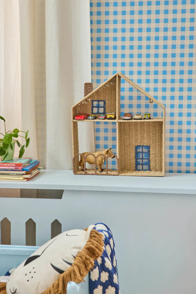 Wicker toy house with miniature cars and a horse figurine on a shelf against a blue checkered wall.