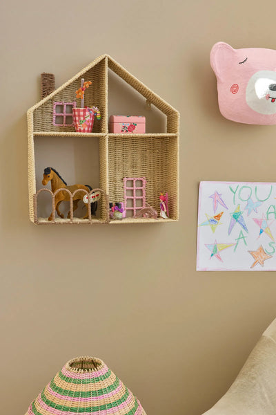 Woven house-shaped shelf with toys against a beige wall, featuring a child's drawing.