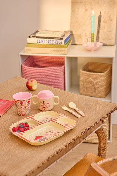 Children's table setting with plates, cups, and utensils on a wooden table.