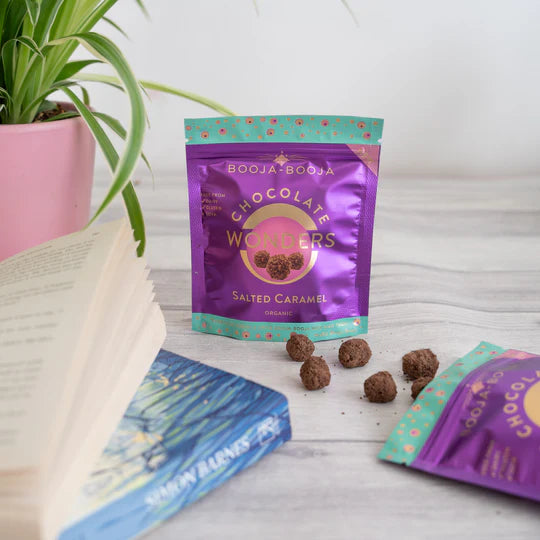 Booja-Booja Chocolate Winners salted caramel chocolate truffles on a wooden surface with packaging and a plant in the background.
