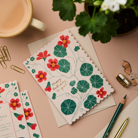 Floral birthday card on a desk with a cup, pen, and plant