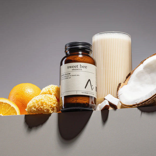 Product with 'sweet bee organics' label surrounded by oranges, honeycomb, and coconut on a grey background