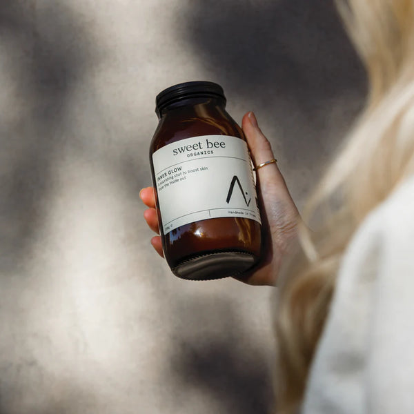 Hand holding a 'sweet bee organics' jar with a blurred background