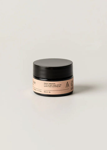 Cosmetic jar with black lid and pink label on a light beige background