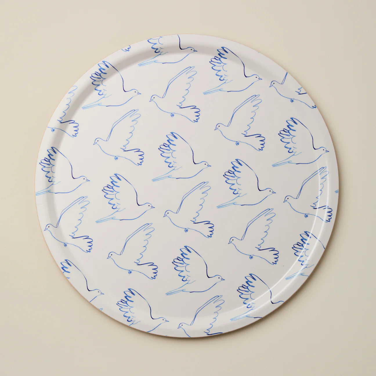 Round tray with blue line art doves against a beige background