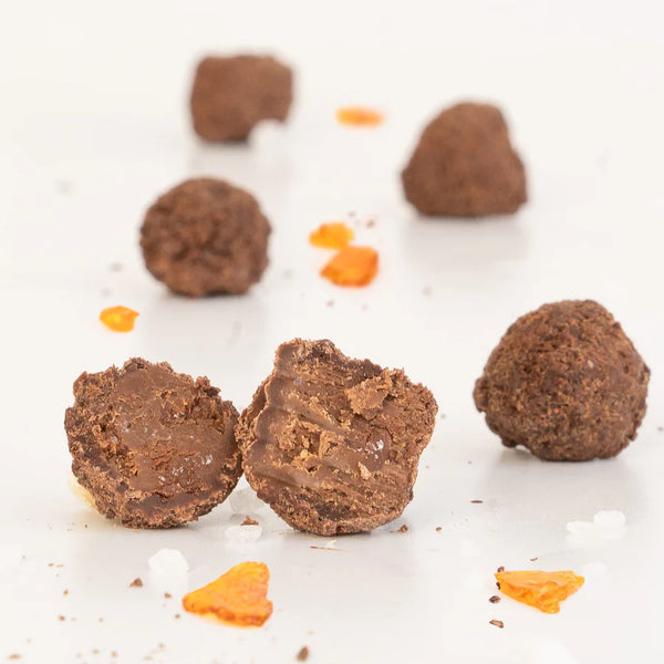 Chocolate truffles with a few broken open on a white surface with orange pieces scattered around.