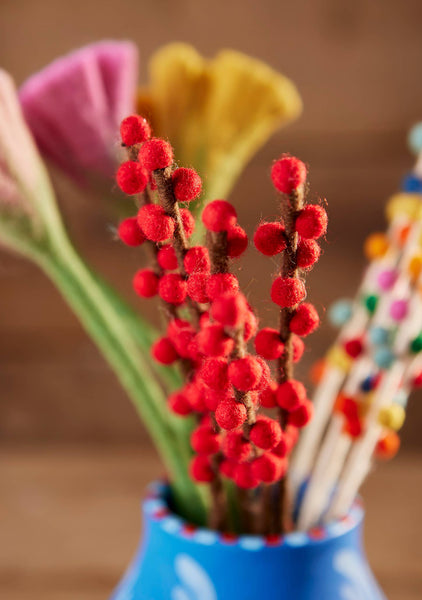 Red floral arrangement in a blue vase with blurred colorful flowers in the background