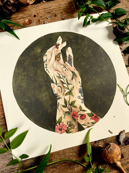 Illustration of tattooed hands with flowers and butterflies on a dark background, surrounded by green leaves and pine cones.