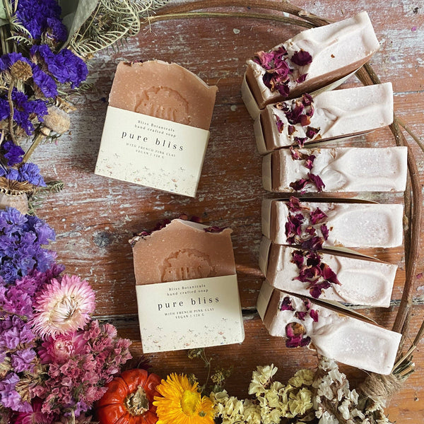 Pure Bliss soap bars on a wooden surface with flowers around