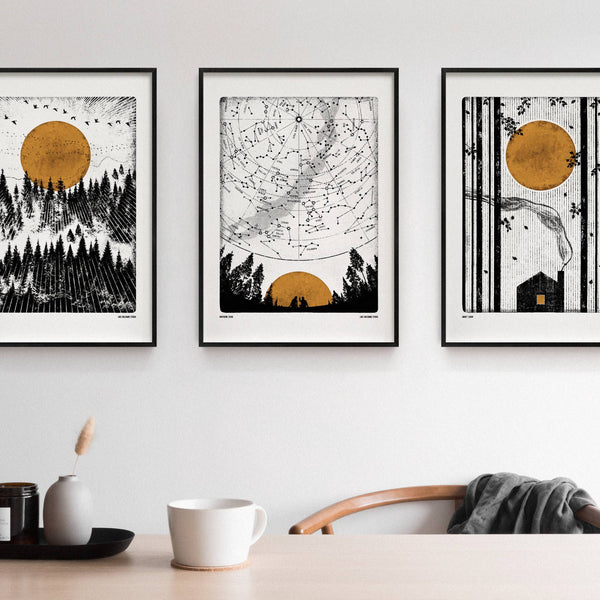 Three framed artworks on a wall above a table with a cup and decorative items.