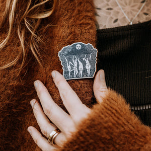 Person wearing a brown sweater with a decorative pin on it.