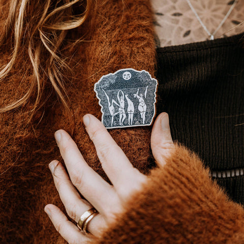 Person wearing a brown sweater with a decorative pin on it.