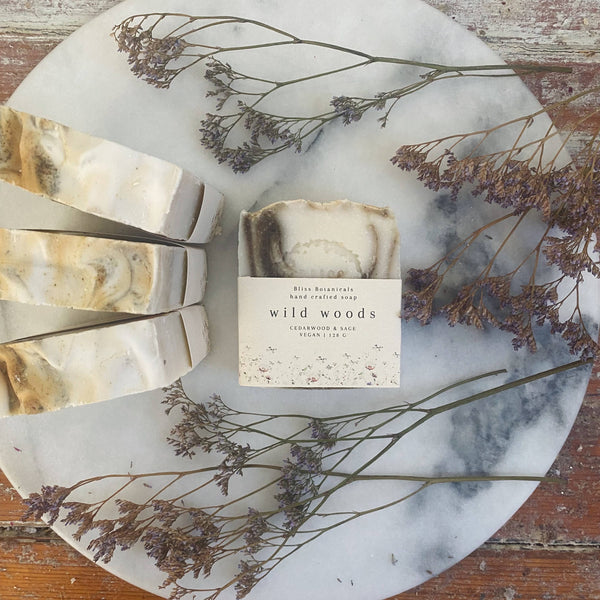 Bar of soap with packaging labeled 'wild woods' on a marble tray with dried flowers.