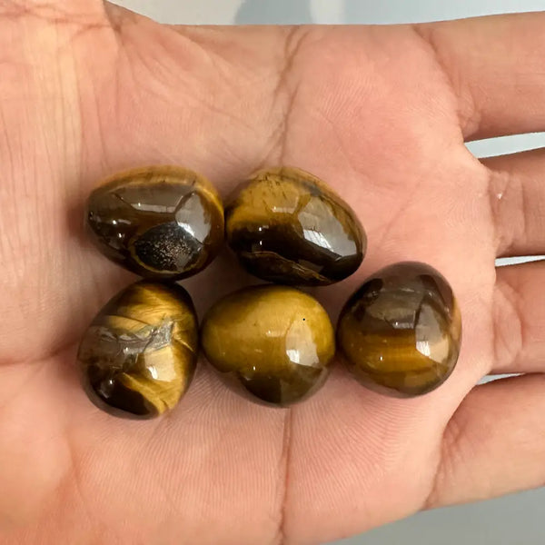 Five tiger's eye gemstones held in a hand against a neutral background