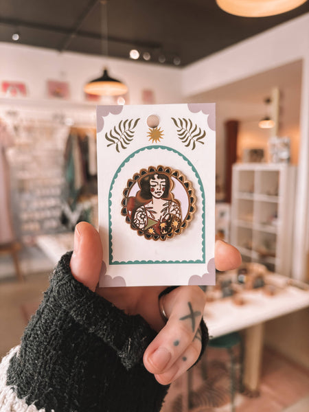 Hand holding a card with a decorative pin badge in an indoor setting.
