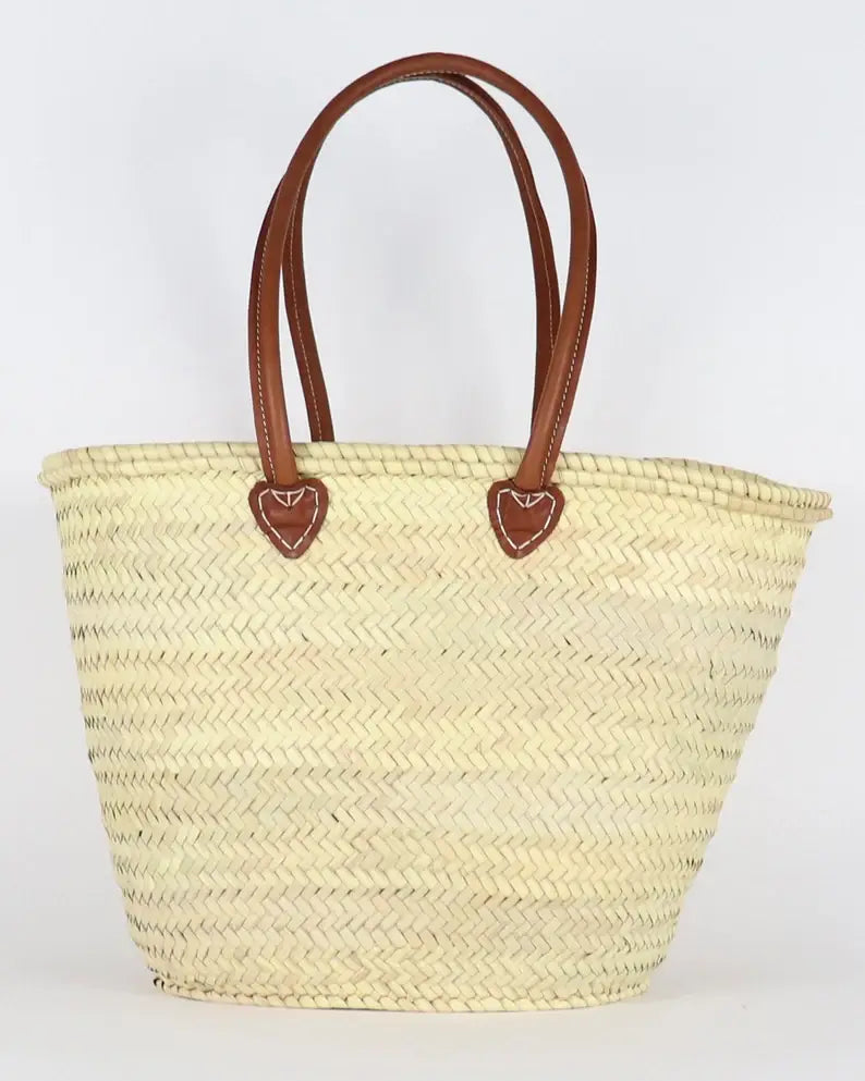 Woven straw tote bag with brown leather handles on a white background