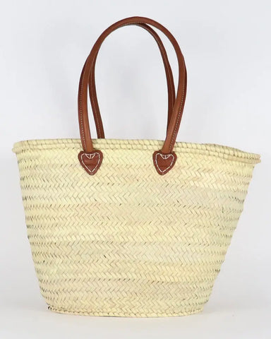 Woven straw tote bag with brown leather handles on a white background
