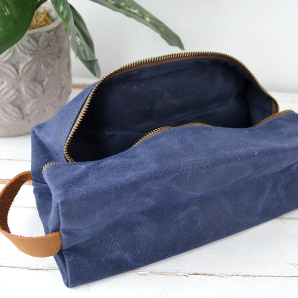 Blue waxed canvas bag with brown leather handle on a white surface