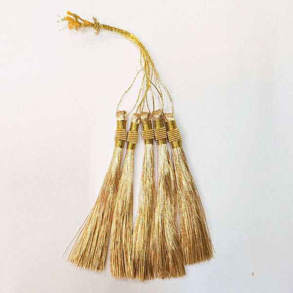 Four decorative gold tassels with metallic gold threads and wrapped bands, hanging from a single gold cord on a plain white background.