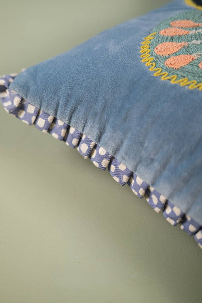 Blue velvet pillow with embroidered design on a green background