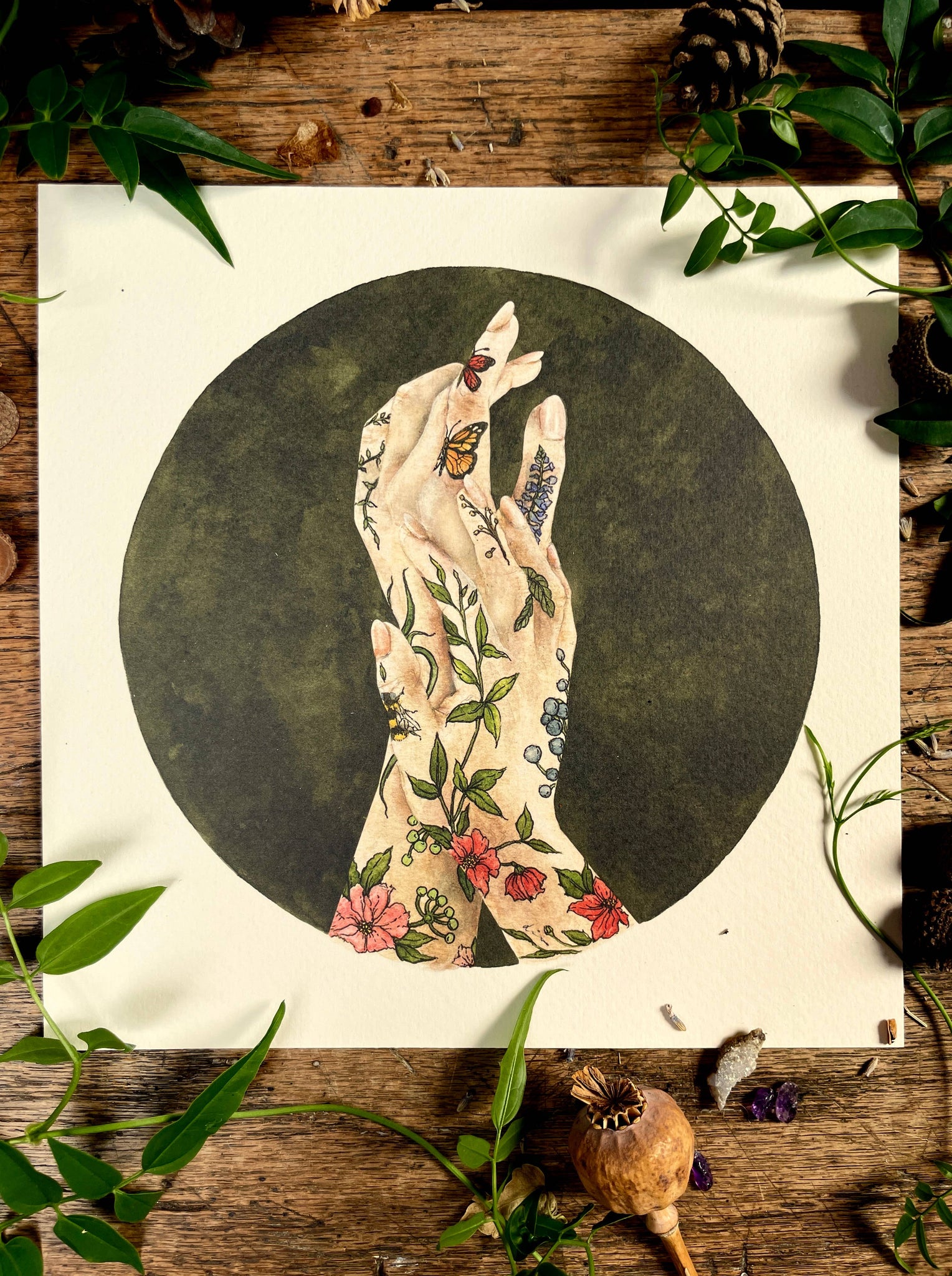 Illustration of tattooed hands with flowers and butterflies on a wooden surface with leaves.