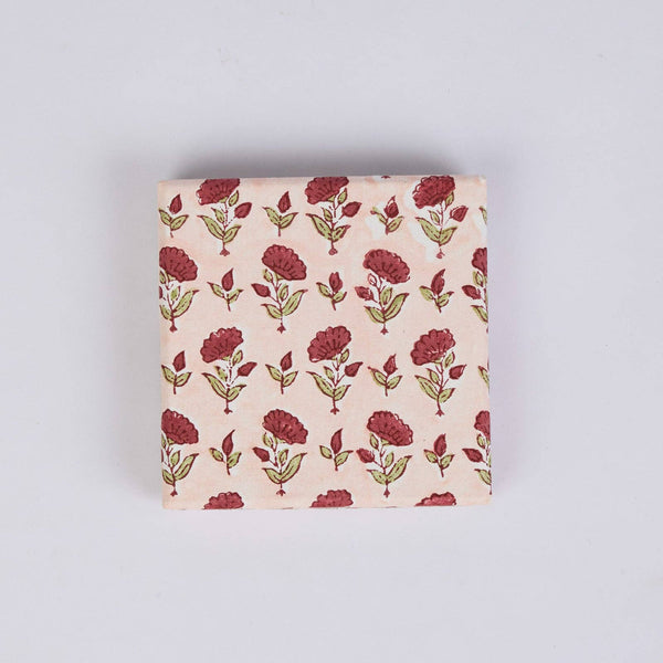A square gift box featuring a repeating block-print floral pattern in dark red and olive green on a light pink background, set against a plain light grey studio backdrop.