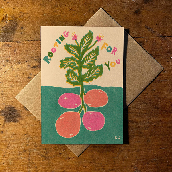 Greeting card with plant illustration and 'Rooting for You' text on a wooden surface