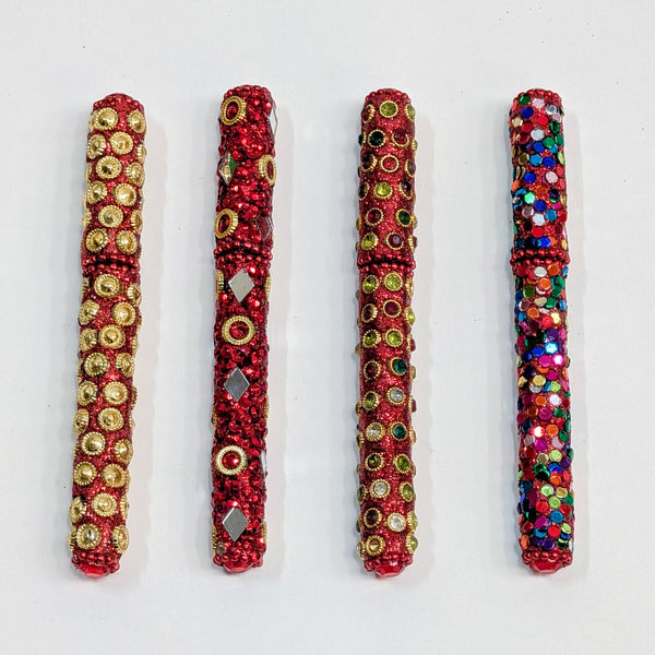Four red sequinned pens arranged vertically on a white background, each decorated with different embellishments including gold circles, silver diamonds, green gems, and multicolour sequins.