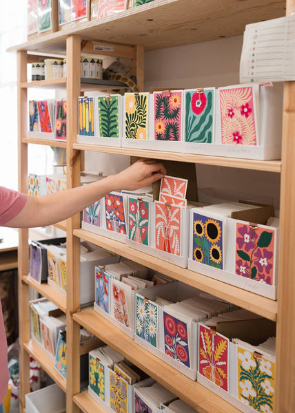 Shelf with colourful greeting cards displayed in boxes and a hand reaching out to select one.