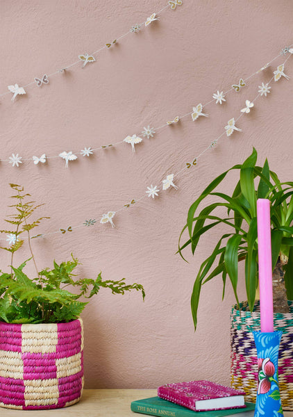 Decorative garland with butterflies on a pink wall, with plants and books in the foreground.