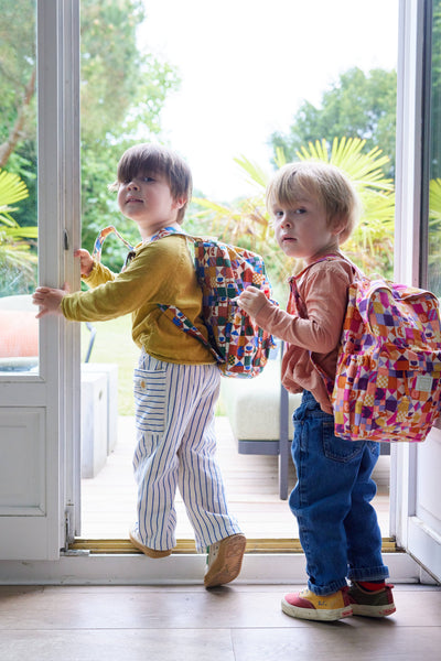 Two children with colourful backpacks standing at a door.