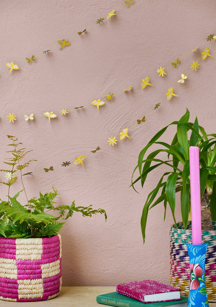 Decorative butterfly garland on a pink wall with plants and books on a table.