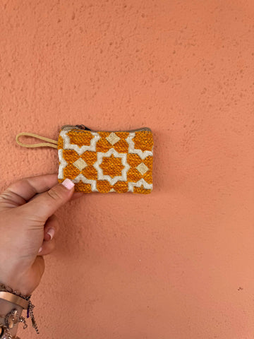 Hand holding a small dark yellow and white patterned pouch against a pink background