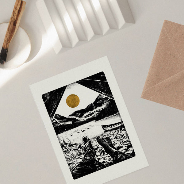 Greeting card with a scenic illustration of mountains and a lake on a white surface.