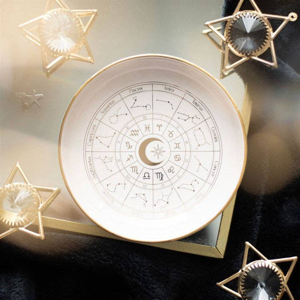 Decorative dish with zodiac design surrounded by star-shaped objects on a dark surface.