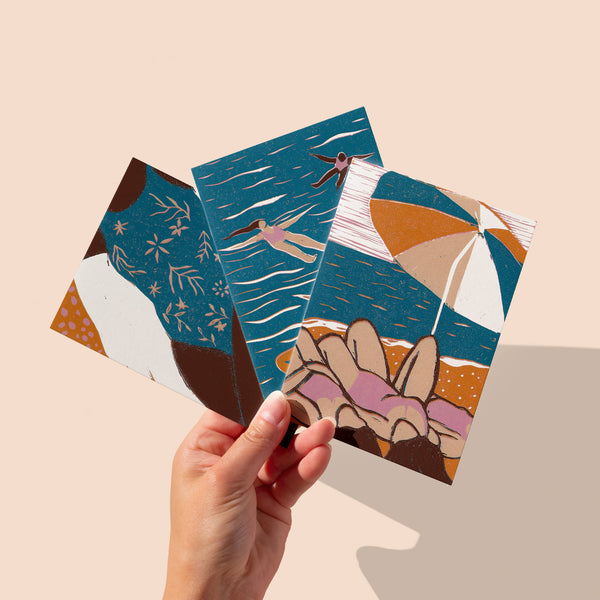 Three artistic postcards held by a hand on a beige background