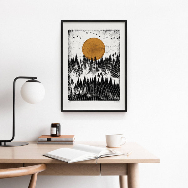 Framed artwork of a forest scene with a sun above, displayed on a wall above a desk.